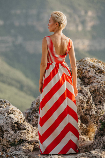 Atraktivní blondýnka dáma v červené a bílé šaty pózuje na útesu. Portrét zezadu. Španělsko - Fotografie, Obrázek