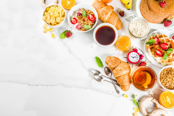 Healthy breakfast eating concept, various morning food - pancakes, waffles, croissant oatmeal sandwich and granola with yogurt, fruit, berries, coffee, tea, orange juice, white background - Photo, Image