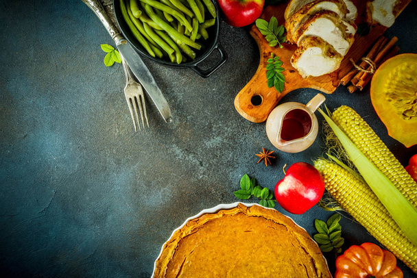 Thanksgiving holiday table with traditional festive food - turkey, pumpkin pie, pumpkins, green beans, cranberry sauce, corn, autumn apples, dark rusty table, top view space for text - Foto, afbeelding