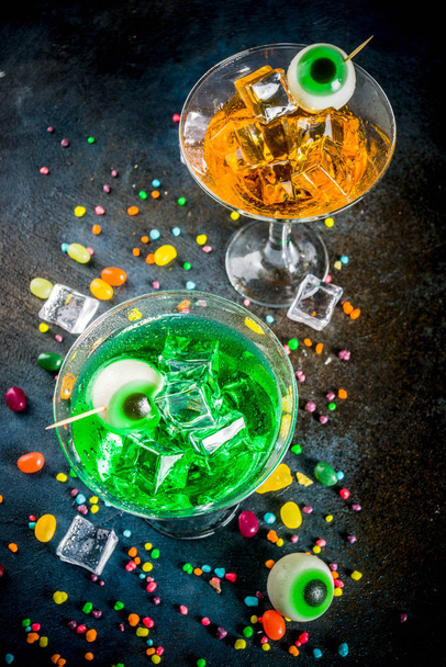 Delizie spettrali per Halloween, un cocktail di martini verde brillante all'arancia con cubetti di ghiaccio e un arredamento di occhi di marshmallow. Su uno sfondo blu scuro, spazio per il testo
 - Foto, immagini