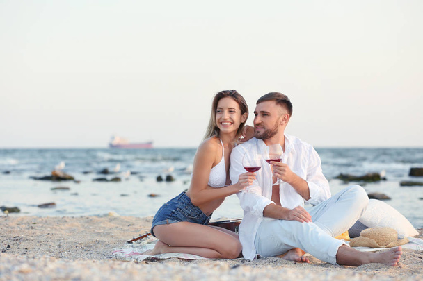 Young couple with glasses of wine on beach - 写真・画像