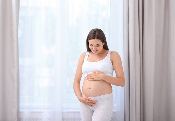 Young beautiful pregnant woman sitting on bed and touching her belly at home - Φωτογραφία, εικόνα
