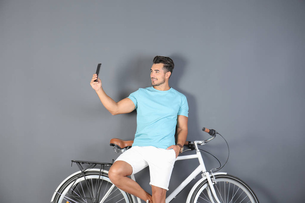 Handsome young hipster man taking selfie with bicycle on color background - Foto, Imagem