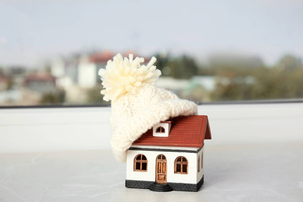 House model with knitted hat on table against blurred background. Heating concept - Photo, Image