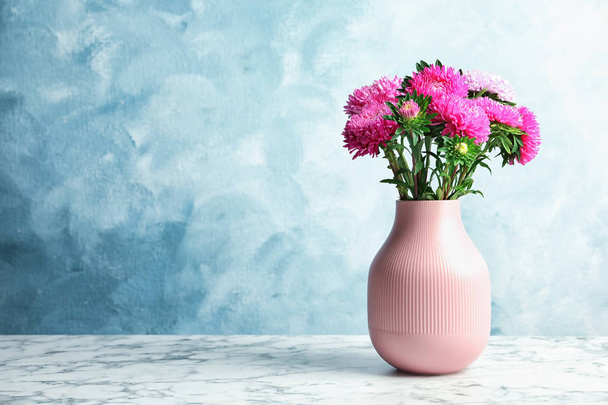 Vase with beautiful aster flower bouquet on table against color background. Space for text - 写真・画像