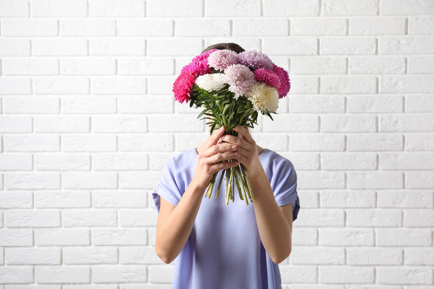 Woman holding beautiful aster flower bouquet against brick wall - Foto, afbeelding