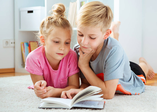 Portrait of two happy children reading a book on the floor at home - Foto, Imagen