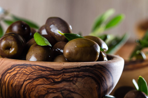 Olives and olive oil in olive wooden bowls on olive wooden cutting board, olive tree branch on wooden rustic background - Foto, Bild