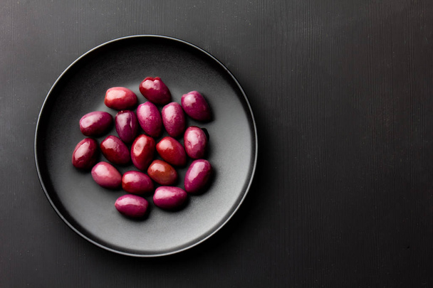 Purple olives on black plate, black wooden background. copy space - Photo, Image