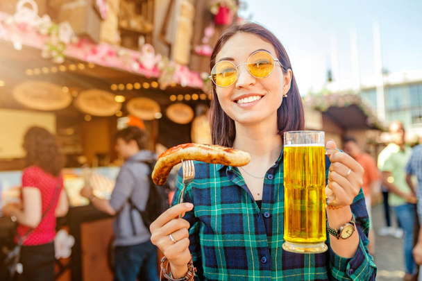 Молодий щасливі азіатських мандрівника жінка їдять смаженою ковбасою та напої кухоль пива в справедливої ринкової площі в Німеччина та пива їжі фестивалю концепції - Фото, зображення