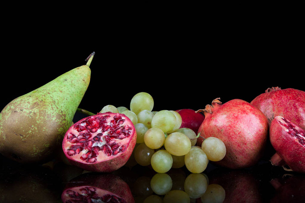 granaattiomenat muiden hedelmien kanssa mustalla taustalla
 - Valokuva, kuva