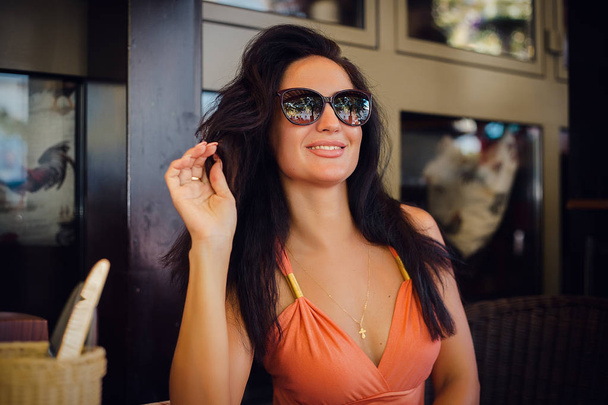 portret uśmiechający się brunetka kobieta siedzi przy stole z odkrytego café noszenia okularów przeciwsłonecznych - Zdjęcie, obraz