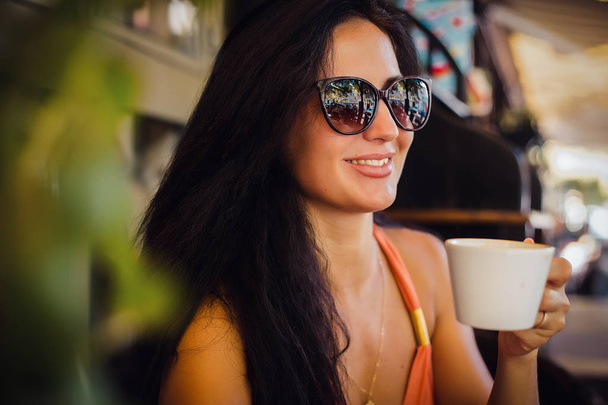 portrait of smiling brunette woman wearing sunglasses and holding coffee cup - Fotografie, Obrázek