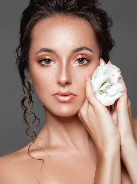 Beautiful young woman with fresh clean skin with white flower on her hand. Treatment and beauty concept. - Foto, immagini