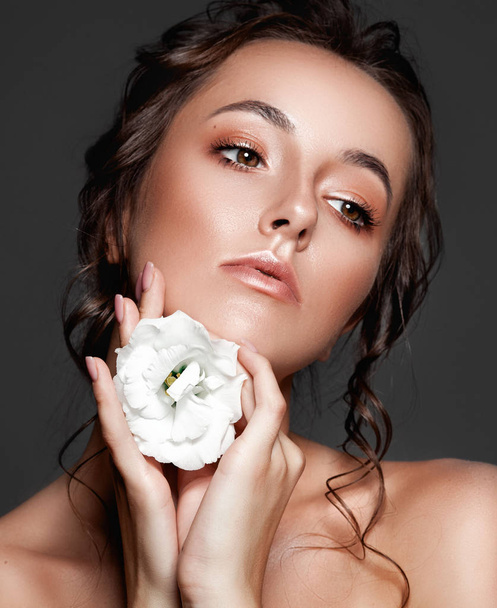Beautiful young woman with fresh clean skin with white flower on her hand. Treatment and beauty concept. - Photo, Image