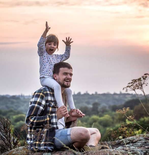 glücklich liebende Familie, Vater hält seine kleine Tochter bei Sonnenuntergang auf seinen Schultern, das Konzept der Familienbeziehungen und Freundschaft - Foto, Bild