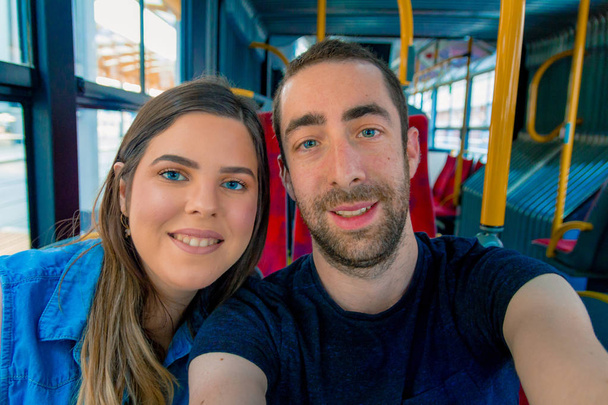 Счастливая пара делает селфи со смартфоном или камерой внутри городского автобуса
. - Фото, изображение