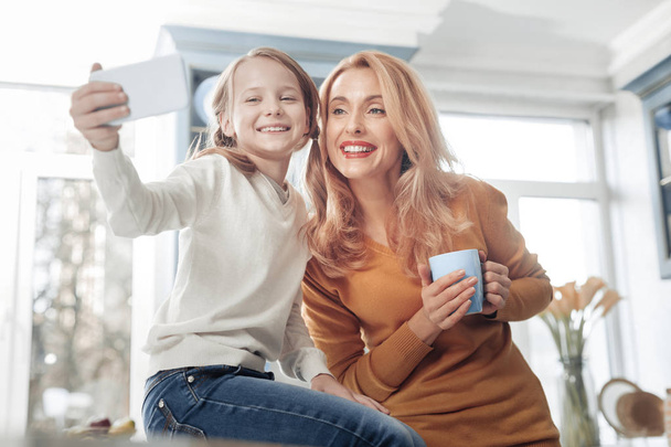 Cheerful schoolgirl being at home with mom - Photo, image