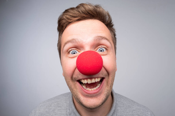 Белый мужчина с сумасшедшим взглядом носит клоунский нос. Концепция счастливого дня рождения, в хорошем настроении
 - Фото, изображение