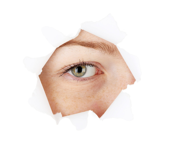 Female eye looking through hole in sheet of paper - Φωτογραφία, εικόνα