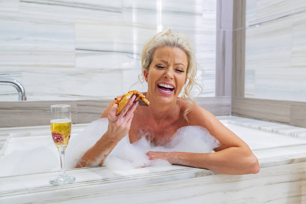 Красива блондинка модель приймає ванну під час їжі піци і пиття шампанського
  - Фото, зображення