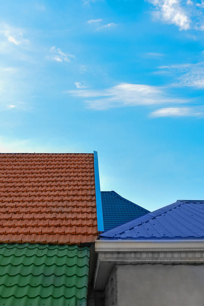 Πολύχρωμα κεραμιδένιες στέγες των σπιτιών ενάντια στον γαλάζιο ουρανό με σύννεφα φόντο σοφίτες πορτοκαλί και πράσινο χρώμα κατακόρυφα. - Φωτογραφία, εικόνα