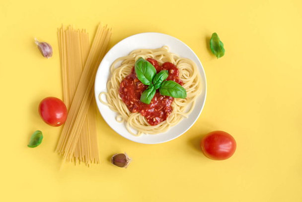 Spaghetti pasta bolognese and ingredients on yellow background, top view. Plate of pasta dish with tomato sauce and basil on creative yellow background. - Foto, imagen