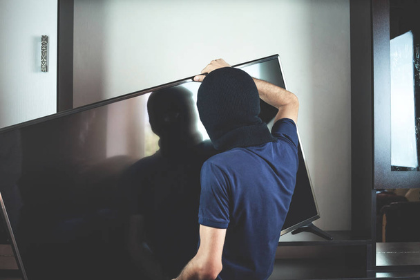 Thief with black balaclava stealing modern expensive television. - Valokuva, kuva
