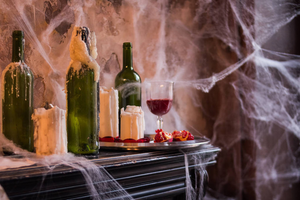 Eerie Cobweb Covered bottles with Candles and Candelabras in Haunted House Setting.interior and decorations for Halloween party.fresh ripe pomegranate, red juice.still life in haunted House.abandoned - Photo, Image