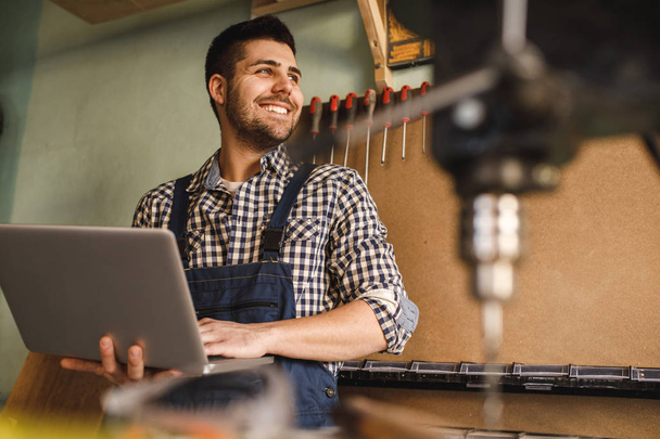Shot of a smiling carpenter using laptop at work in workshop. - Valokuva, kuva