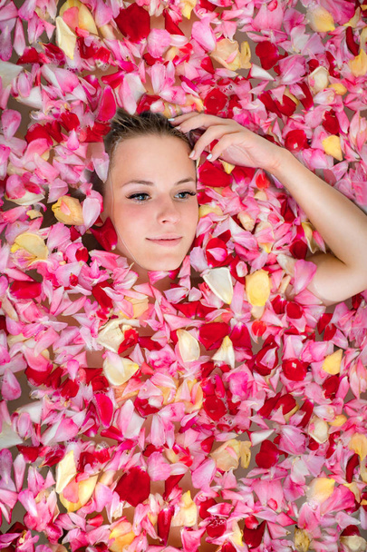 Face of a young girl among rose petals in bath. Spa, wellness or body care concept. - Photo, Image