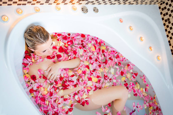 Young beautiful woman relaxing in a bathtub full of rose petals. Spa, wellness or body care concept. - Photo, Image