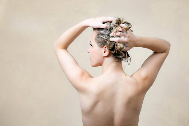 Gorgeous girl takes shower and washing her long hair with shampoo. Back view. On light background - Foto, afbeelding