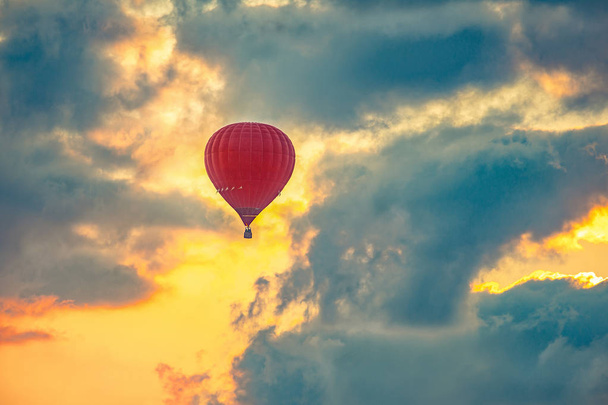 Balão de ar quente vermelho voando no céu bonito, durante o nascer do sol
. - Foto, Imagem