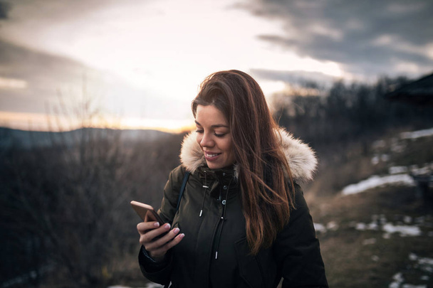 Beautiful girl enjoying a mountain walk and holding her mobile phone. - Valokuva, kuva