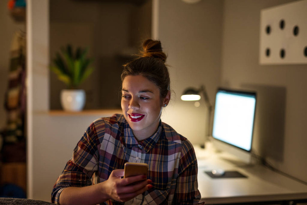 Portrét usměvavá mladá podnikatelka pomocí mobilního telefonu pozdě v noci. - Fotografie, Obrázek