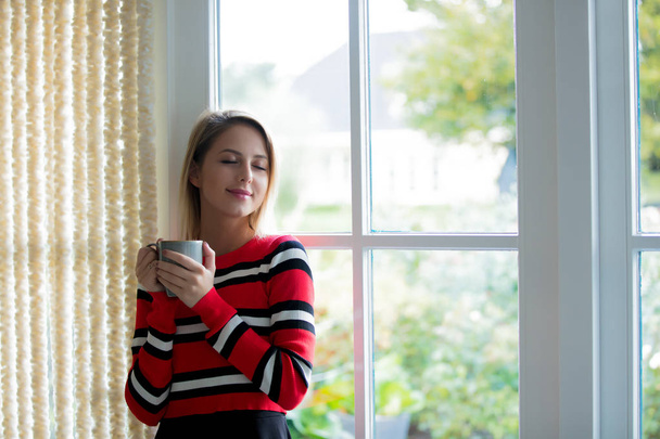 Νεαρό κορίτσι με φλιτζάνι καφέ να μείνετε κοντά σε παράθυρο - Φωτογραφία, εικόνα