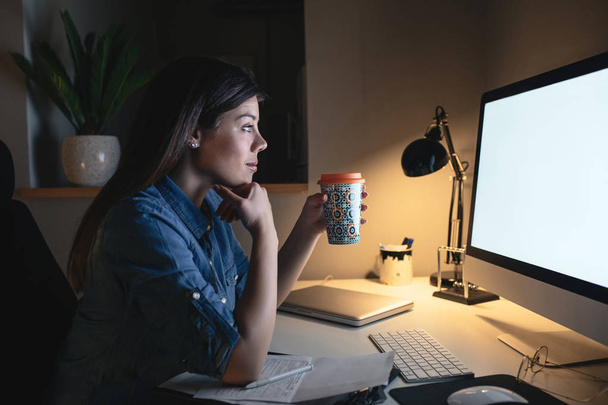 Portrait of a hardworking woman working on a computer late at night while drinking coffee. - Foto, Imagem