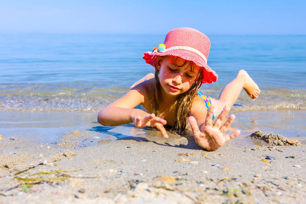 Niña acostada sobre su vientre en aguas poco profundas, ella está dibujando en la arena con los dedos, playa
. - Foto, imagen