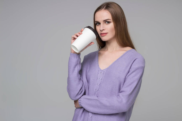 Young model long-haired blond girl in blue purple lilac jamper holds paper plastic coffee glass drinking - Fotó, kép