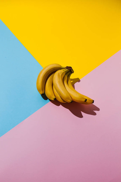 青とピンクと黄色の背景の上の黄色のバナナ - 写真・画像