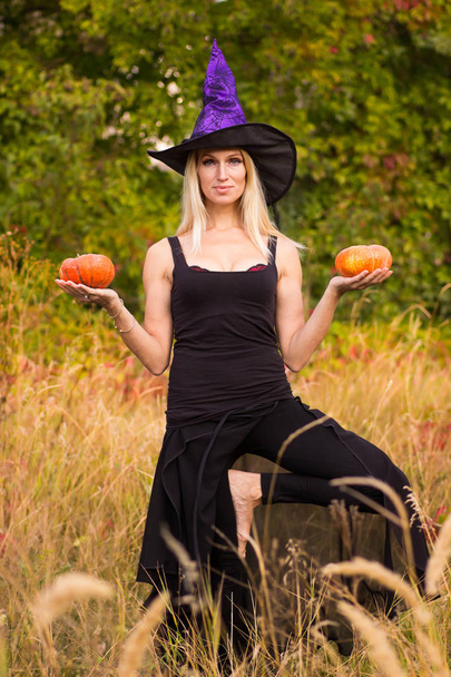 Sportovní žena v Halloween kostýmu čarodějnice cvičení pozic jógy s dýně ve svých rukou - Fotografie, Obrázek
