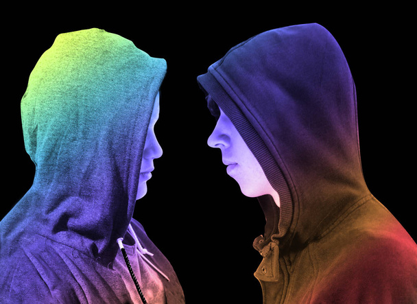 Two troubled teenage boys with black hoodie standing in front of each other in profile isolated on black background. Creative colorful lighting. - Photo, Image