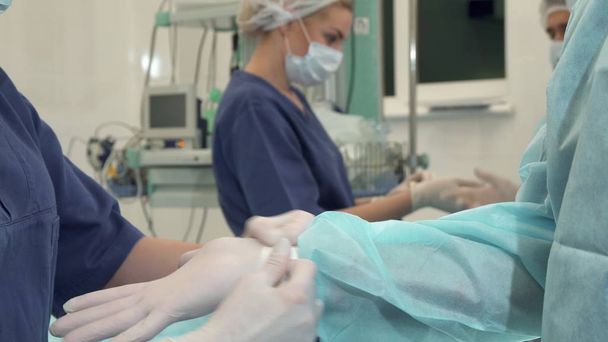 Nahaufnahme einer Krankenschwester, die einen Sterilisationshandschuh an der Hand des Arztes trägt. junge Ärztin, die Anweisungen vom Operationsleiter erhält. Operationsteam bereitet sich auf die Operation des Patienten vor - Foto, Bild