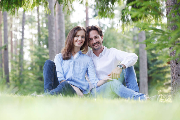 Happy couple sitting on grass in summer park - Фото, зображення