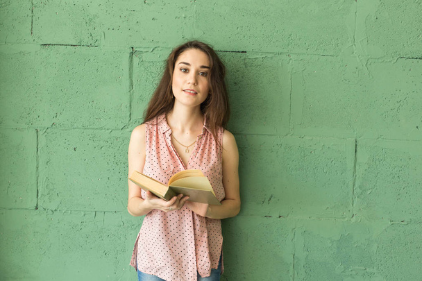 Literature, education, people concept - Female student in reading the book over the green wall - Foto, Imagem