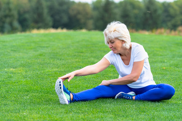 Mujer mayor con ropa deportiva ejercitándose sobre hierba verde en el parque
 - Foto, imagen