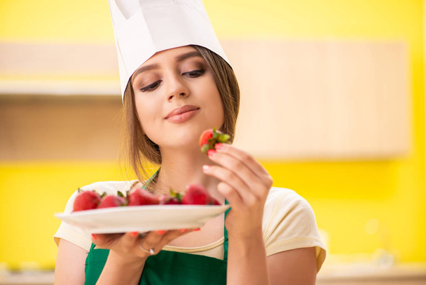 Young female cook eating strawberries - Фото, изображение