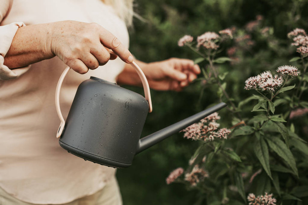 Focus on hand of aged woman with watering can - Foto, afbeelding
