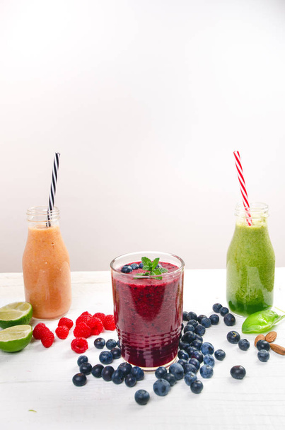 Blueberry, spinachy and orange smoothie on a wooden white background. Glasses of smoothie with berry and mint. Berry, leaf and lime, raspberries on a table. Fruit Healthy food. Breakfast. - Фото, зображення